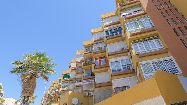 Un edificio de varios pisos con balcones, unidades de aire acondicionado y una palmera en primer plano.