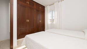 Een slaapkamer met een grote kledingkast, twee bedden en een raam met gordijnen.