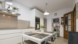 A modern kitchen with white cabinetry, a built-in oven, and a dining table with cushioned chairs. - Casa Del Olivo in Algeciras (Algeciras)