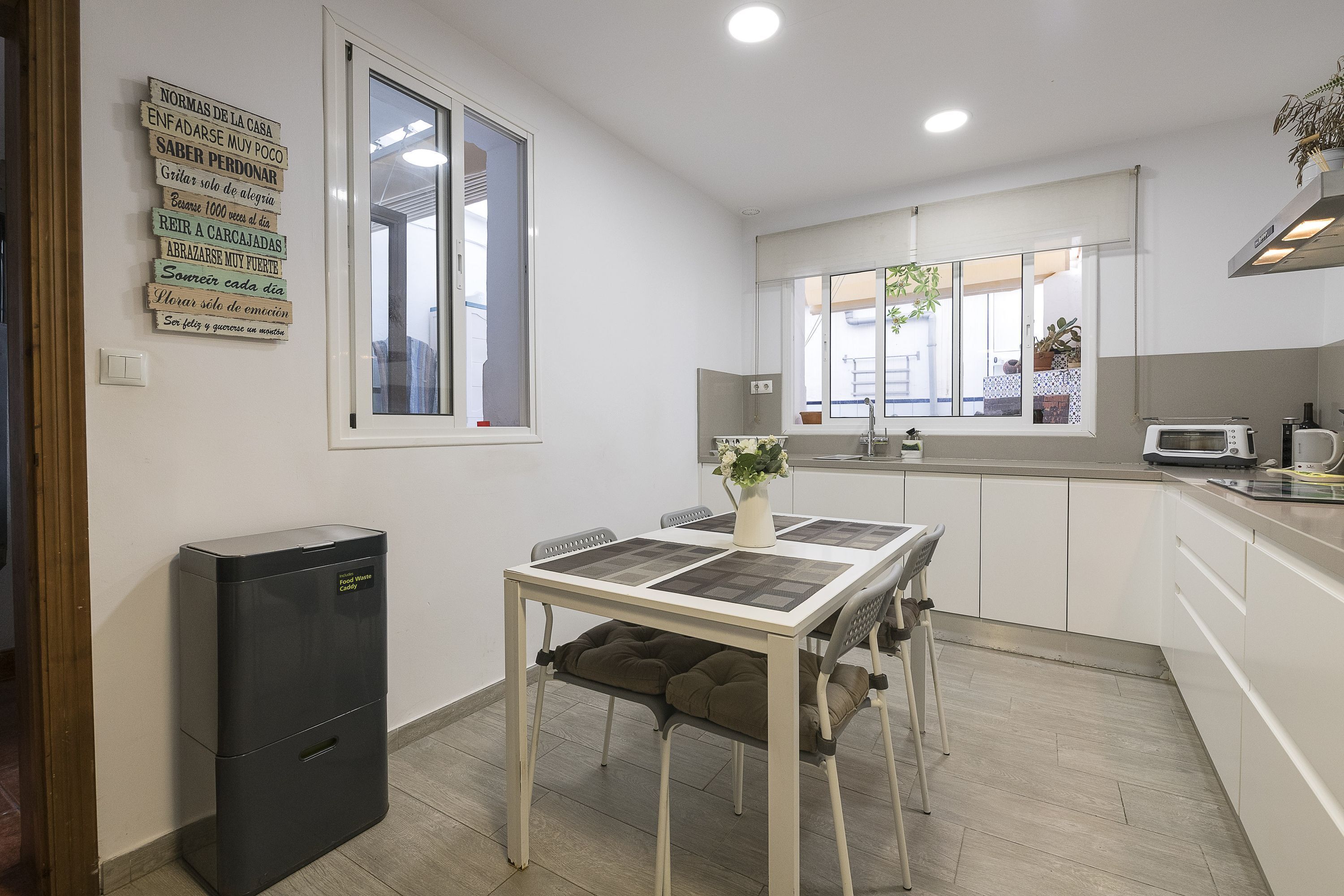 A compact kitchen with a dining table, a trash bin, and a window.