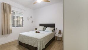 Een slaapkamer met een bed, nachtkastje, raam met gordijnen en een plafondventilator.