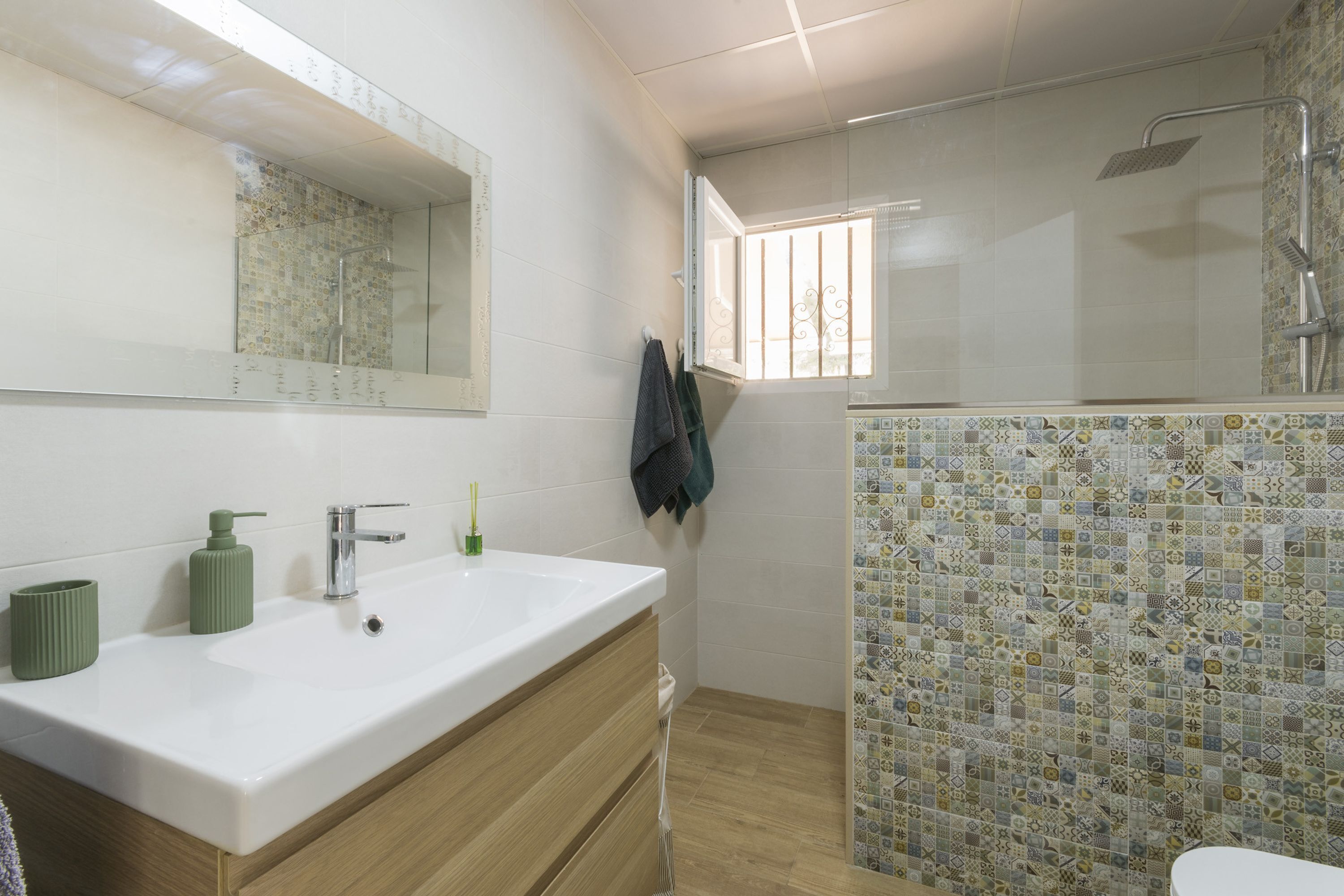 Ein Badezimmer mit einem weißen Waschbecken, einem grünen Seifenspender und einer Dusche mit Glastür.