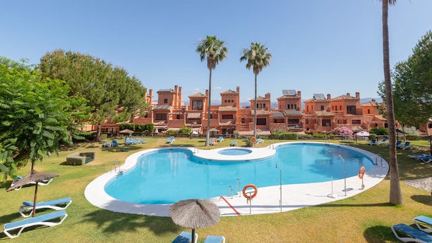 A swimming pool surrounded by lounge chairs and palm trees, with a building in the background. - Clipper in Alhaurin de la Torre (Alhaurin de la Torre)