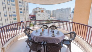 Ένα μπαλκόνι με ένα τραπέζι στρωμένο για τέσσερα άτομα, περιτριγυρισμένο από καρέκλες, με θέα την πόλη, τα κτίρια και έναν δρόμο.