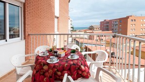 Un balcone con un tavolo apparecchiato per due, sedie di plastica bianca e una tovaglia con un motivo a mele rosse.