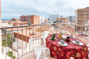 A balcony with a table set for two, white chairs, and a view of the cityscape and sea.