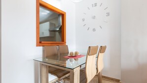 A dining area with a glass table, wooden chairs, a wooden-framed window, and a wall clock. - Casa Carmen in Bah a Dorada (Estepona)