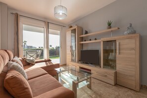 A modern living room with a sofa, glass coffee table, TV, wooden cabinet, and a view through the glass door.