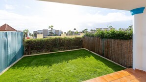 A backyard with a green lawn, a wooden fence, and a tiled patio area. - Casa Carmen in Bah a Dorada (Estepona)