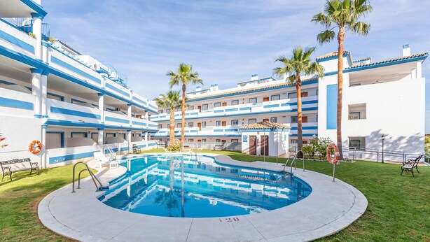 A hotel with a central swimming pool, multiple balconies, and palm trees. - Casa Carmen in Bah a Dorada (Estepona)