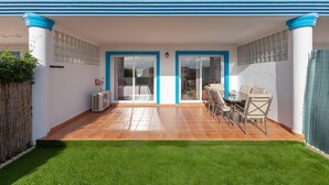A covered patio with a dining table and chairs, a small air conditioning unit, and a green lawn. - Casa Carmen in Bah a Dorada (Estepona)