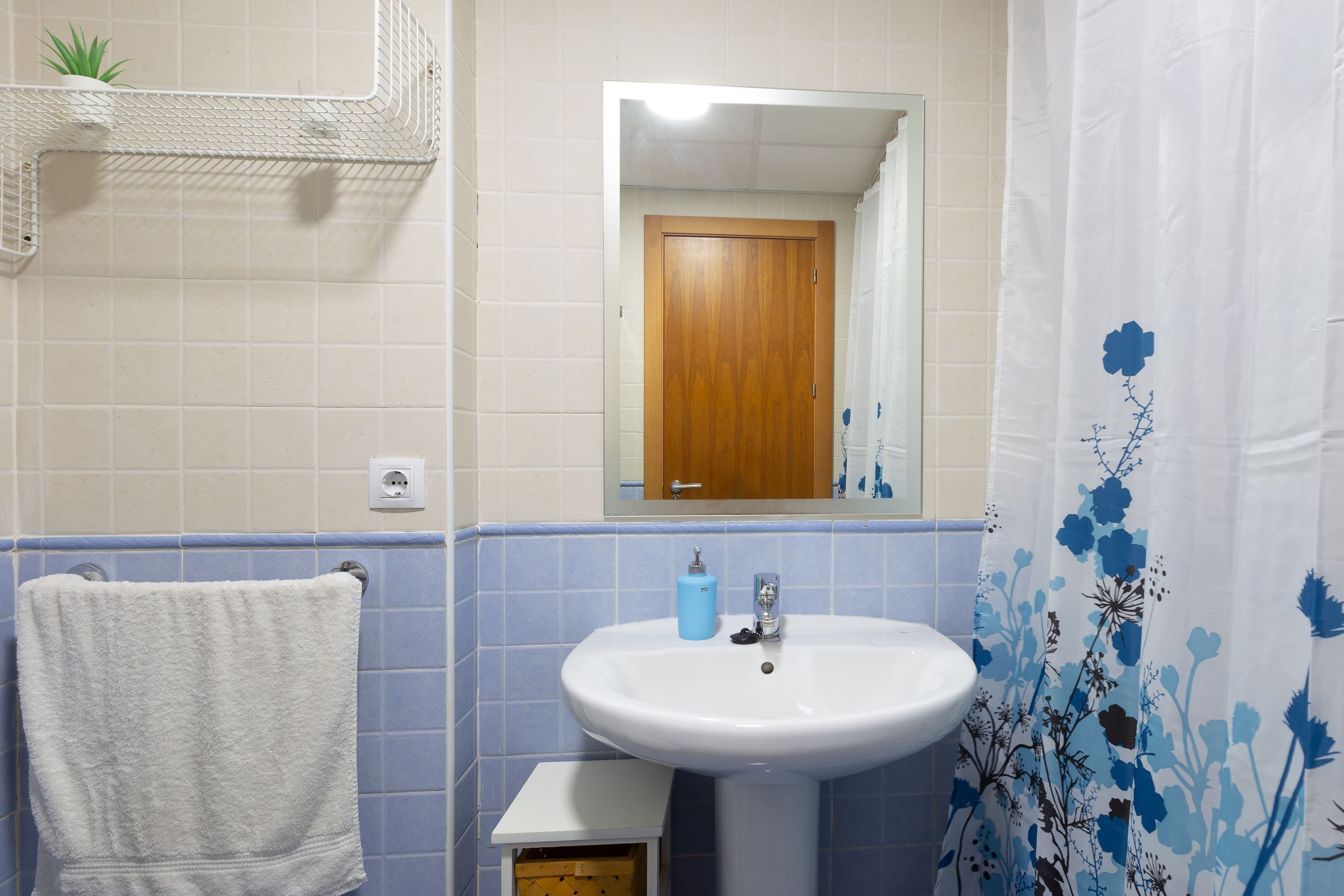 Ein Badezimmer mit einem weißen Waschbecken, blau gefliesten Wänden, einer Holztür und einem Duschvorhang mit Blumenmuster.