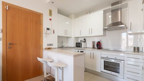 Une cuisine moderne avec des meubles blancs, un four en acier inoxydable, un four à micro-ondes et une porte en bois.