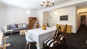 A dining area with a white table, striped chairs, and a fruit centerpiece. A grey sofa and wooden cabinet are in the background. - Samba in Gandia With 3 Bedrooms and 1 Bathrooms (Gandia)