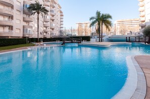 A swimming pool with a palm tree and a bridge, surrounded by apartment buildings. - Para so in Grau i Platja (Gandia)