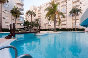 A swimming pool surrounded by palm trees and a multi-story building with balconies. - Para so in Grau i Platja (Gandia)
