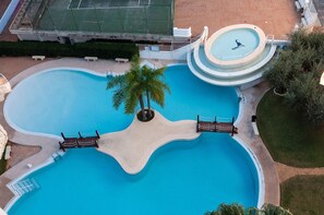 An aerial view of a swimming pool with a unique wavy edge design, surrounded by palm trees and a small circular hot tub. - Para so in Grau i Platja (Gandia)