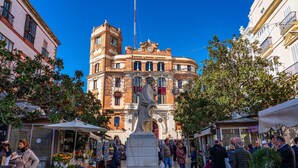 A public square with a fountain, a statue, and a building with a clock tower.