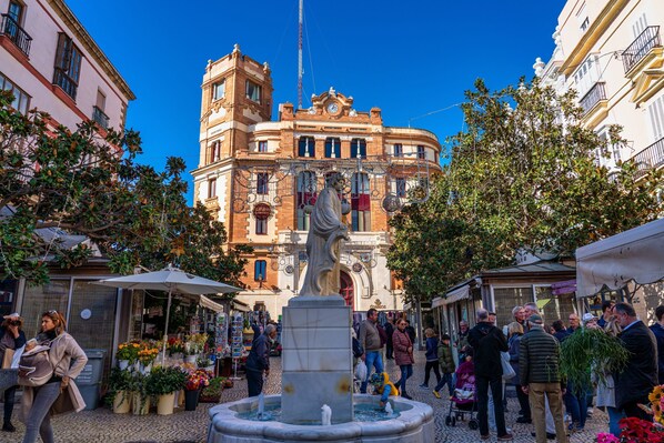 A public square with a fountain, a statue, and a building with a clock tower.