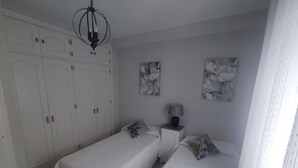 A bedroom with two single beds, a wardrobe, a nightstand with a lamp, and floral wall art.