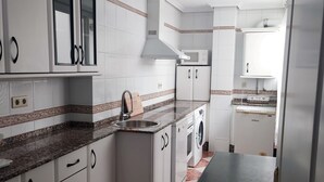 A compact kitchen with white cabinets, a granite countertop, a microwave, a sink, and a washing machine.
