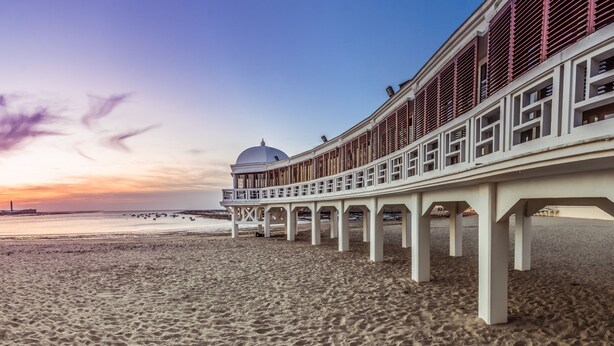 A beach promenade with a white structure featuring a dome and red railings.