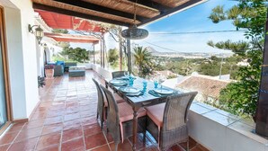 Terrassa exterior amb taula preparada per dinar, cadires de vimet i vista a un paisatge urbà.