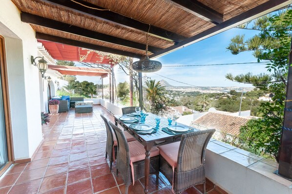 An outdoor patio with a table set for dining, wicker chairs, and a view of a cityscape. - Tramuntana in Trencall (Javea)