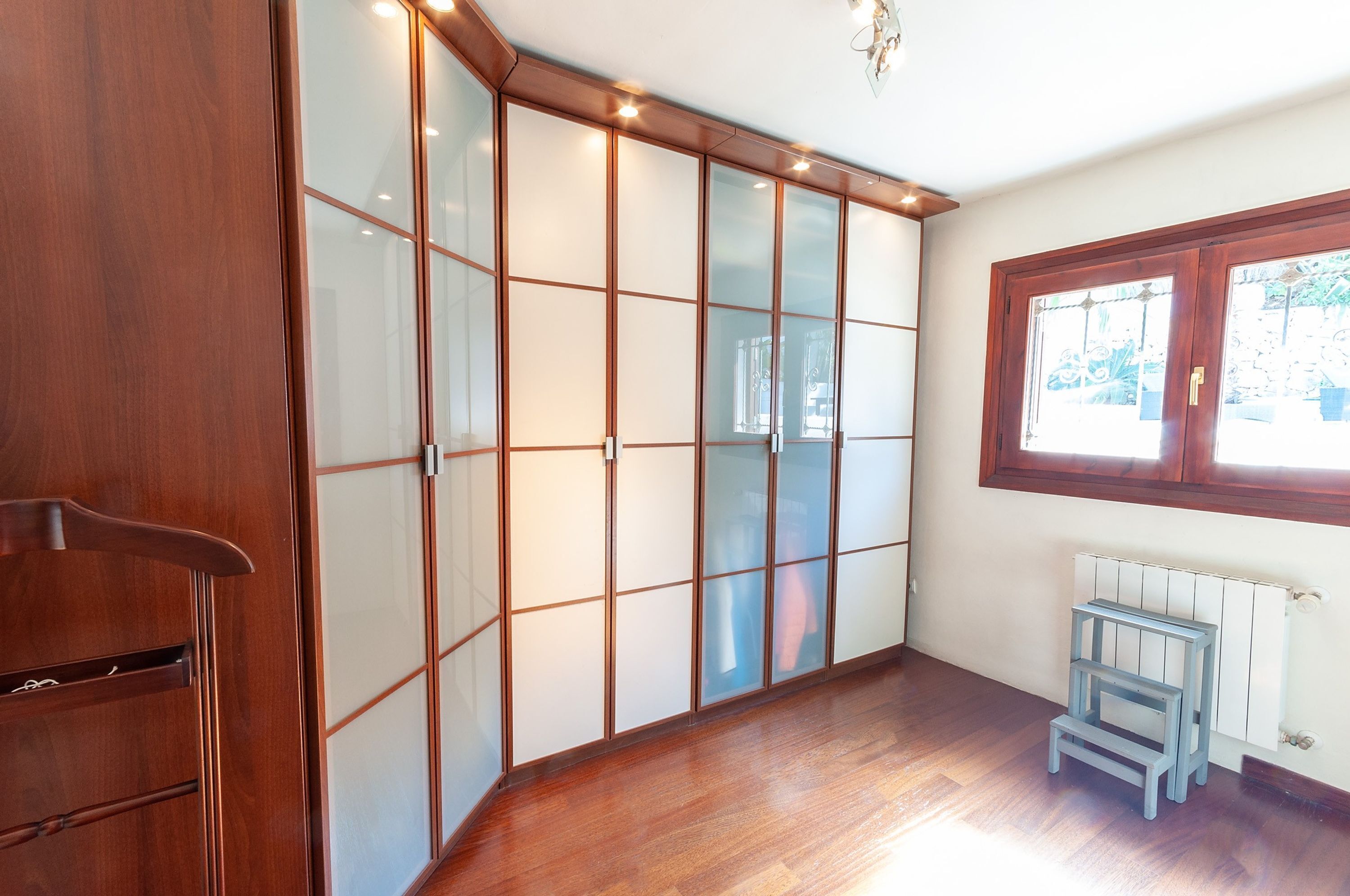 Une pièce avec une armoire en bois, un radiateur et une fenêtre donnant sur un espace verdoyant.