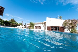 A swimming pool with a clear blue sky above, surrounded by white buildings with brown shutters and a palm tree. - Tramuntana in Trencall (Javea)