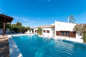 A swimming pool surrounded by a white building with brown shutters, a pergola, and a clear blue sky. - Tramuntana in Trencall (Javea)