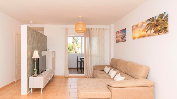 Un salón con un sofá color crema, un televisor sobre un mueble bajo, una lámpara y un cuadro en la pared.
