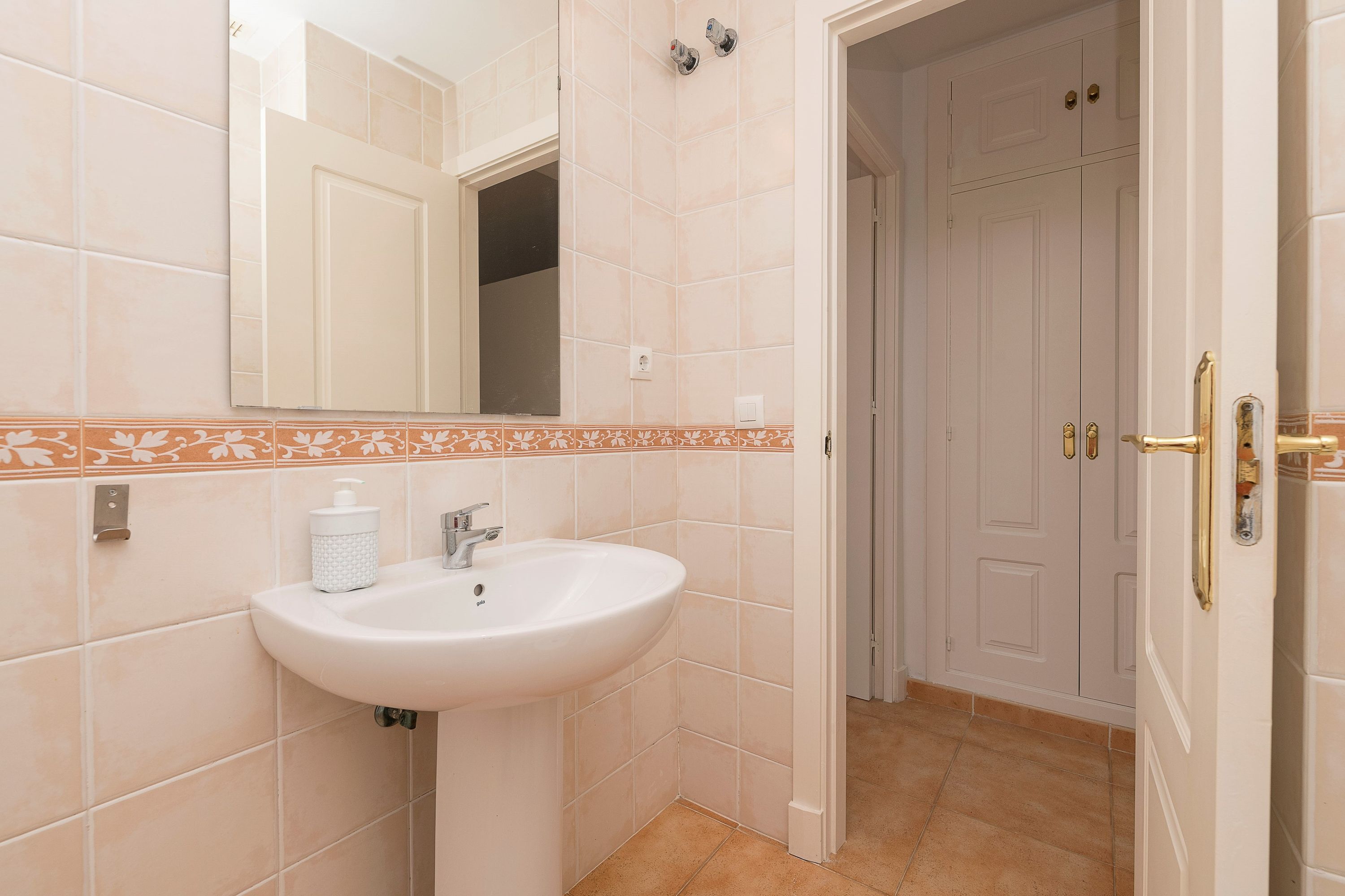 Un baño con un lavamanos blanco, un espejo y una puerta que da a otra habitación.