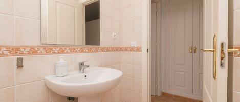 Un baño con un lavamanos blanco, un espejo y una puerta que da a otra habitación.