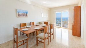 A dining area with a wooden table set for four, chairs with cushioned seats, a painting on the wall, and a view of the sea through a glass door. - Turia in Tavernes de la Valldigna (Tavernes de la Valldigna)