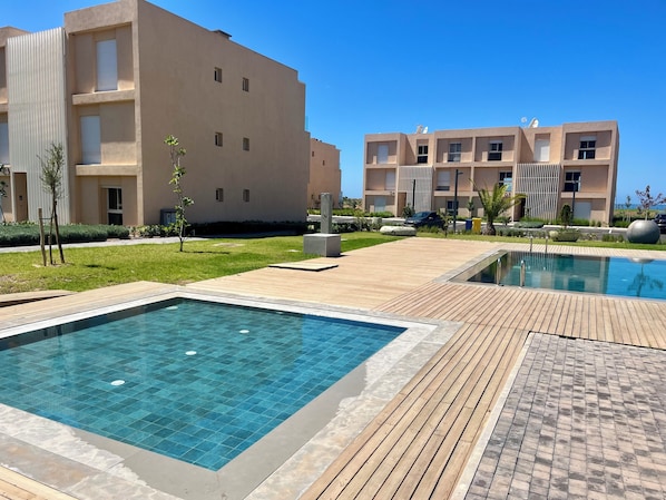 A modern residential complex with a swimming pool and wooden deck.