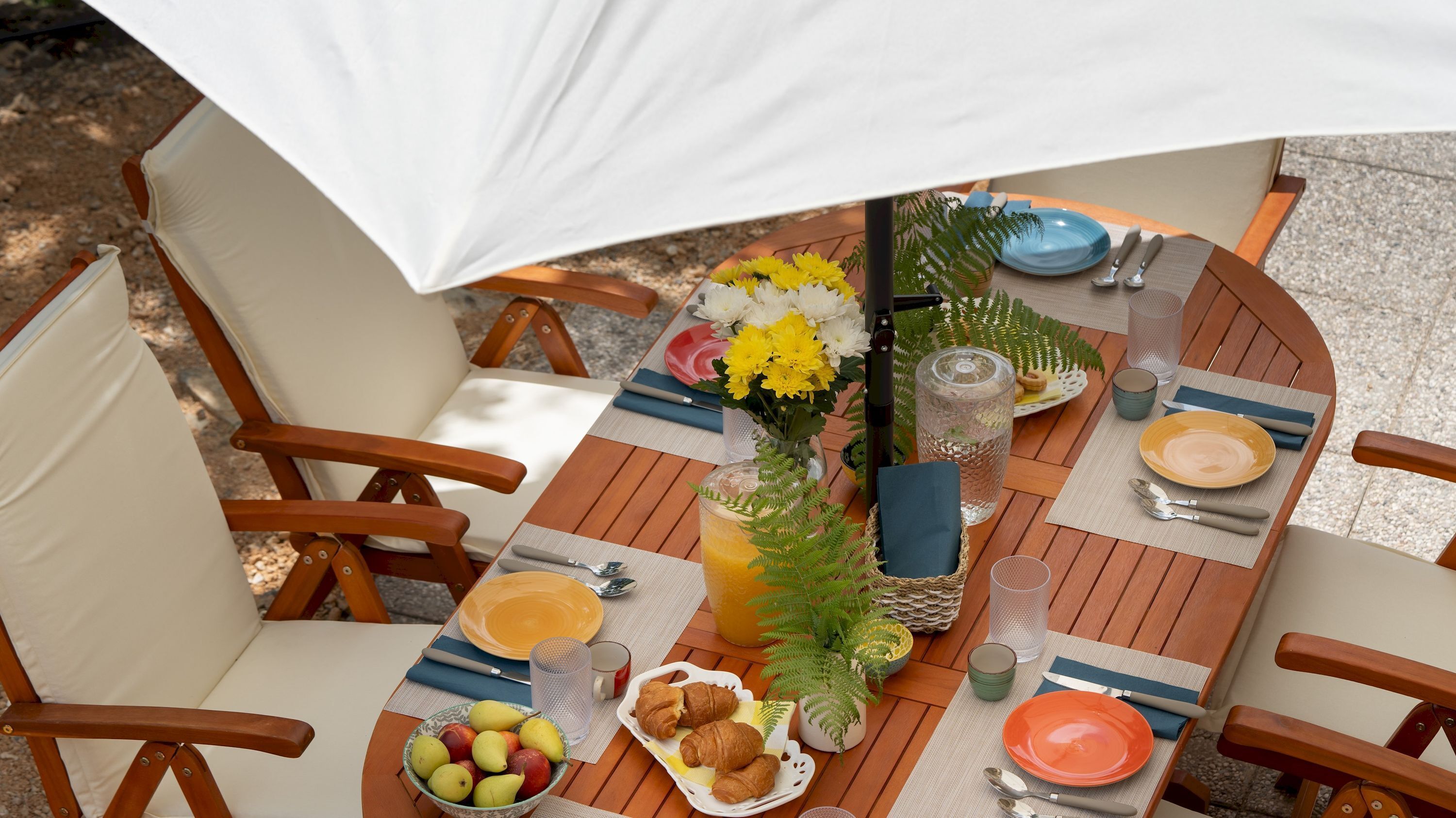 A round wooden table with a white umbrella, surrounded by wooden chairs.