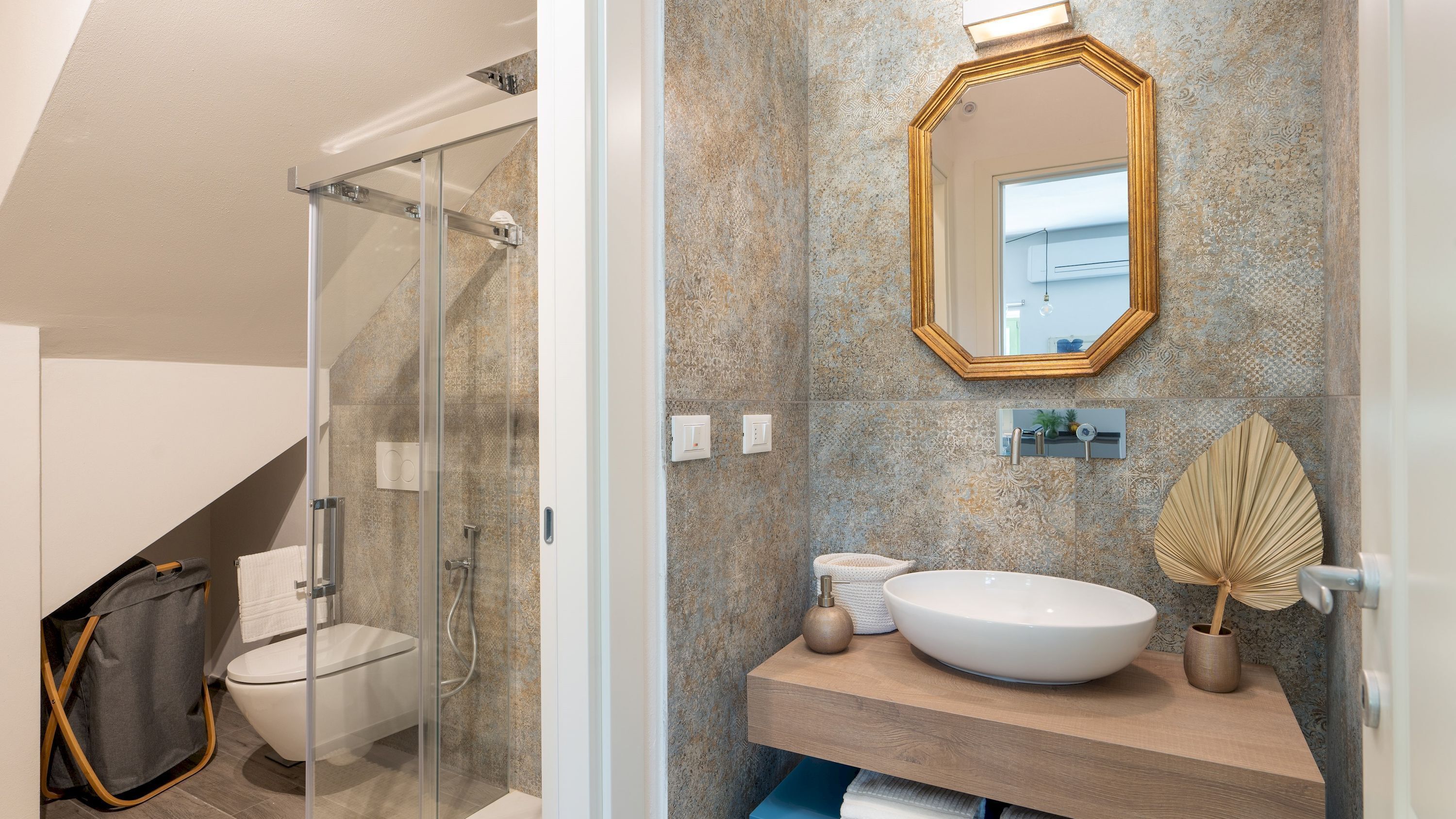 Une salle de bain moderne avec une douche à parois de verre, des toilettes sur pied, un grand lavabo ovale et un miroir décoratif.