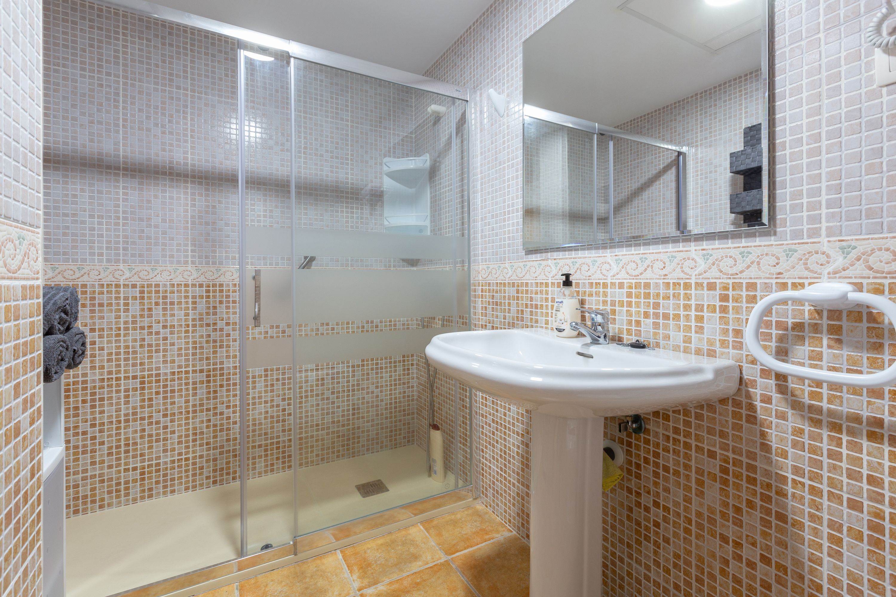 A bathroom with a glass-enclosed shower, a sink with a mirror above it, and tiled walls.