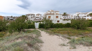 Un camino que lleva a una zona residencial con edificios blancos, palmeras y un paisaje arenoso.