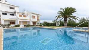 Una piscina con un diseño de mosaicos, rodeada por un edificio blanco con balcones y una palmera.