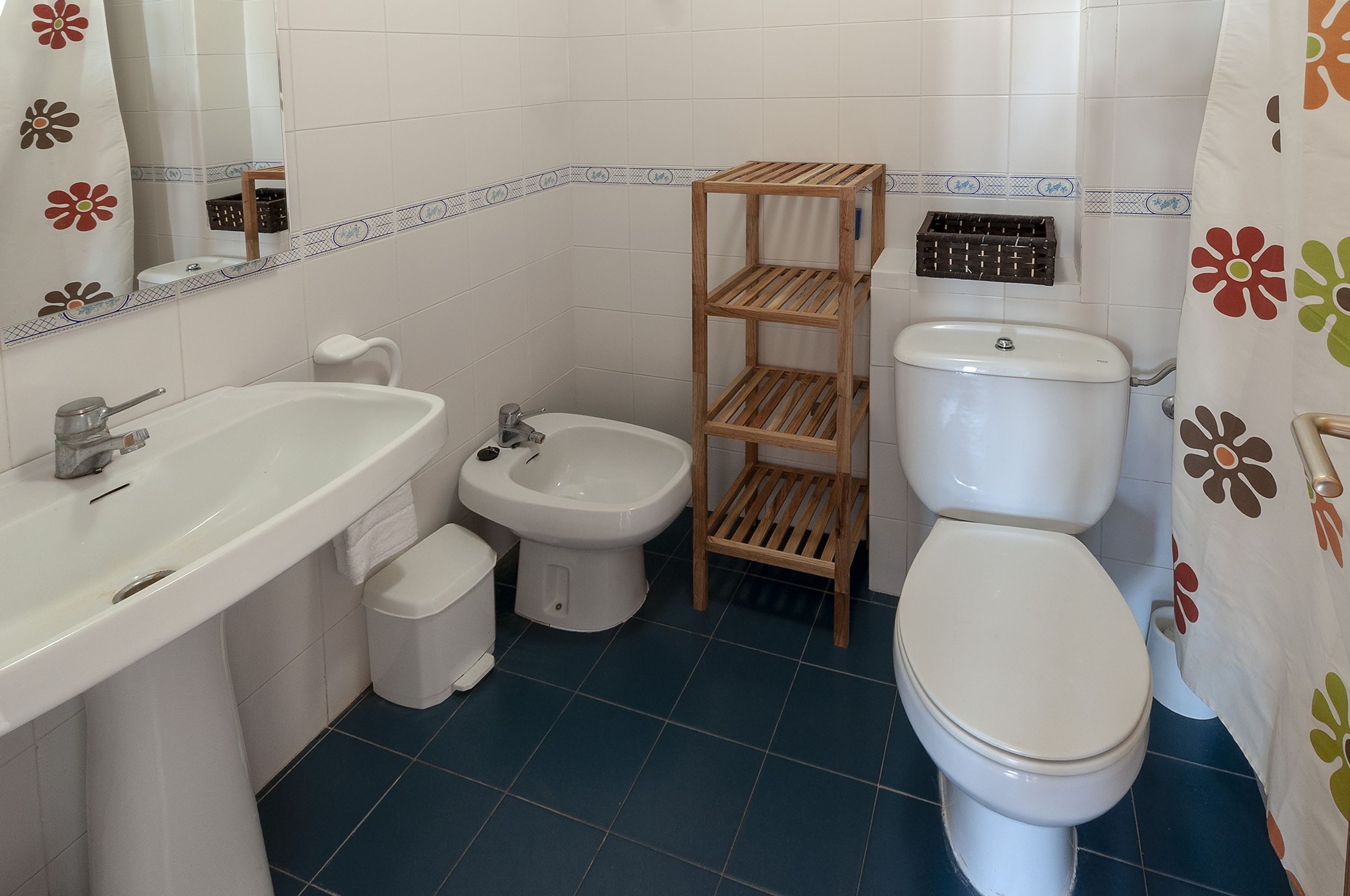 A bathroom with a sink, bidet, toilet, and wooden shelves.