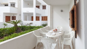 Un balcón con una mesa blanca para cuatro personas, rodeado de sillas blancas, y vistas a un edificio blanco con contraventanas de madera.