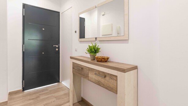 Un couloir avec une porte noire, une console en bois surmontée d’un miroir et une plante en pot.