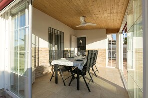 Un espace de restauration en plein air avec une table et des chaises, un ventilateur de plafond et une vue sur l’extérieur.