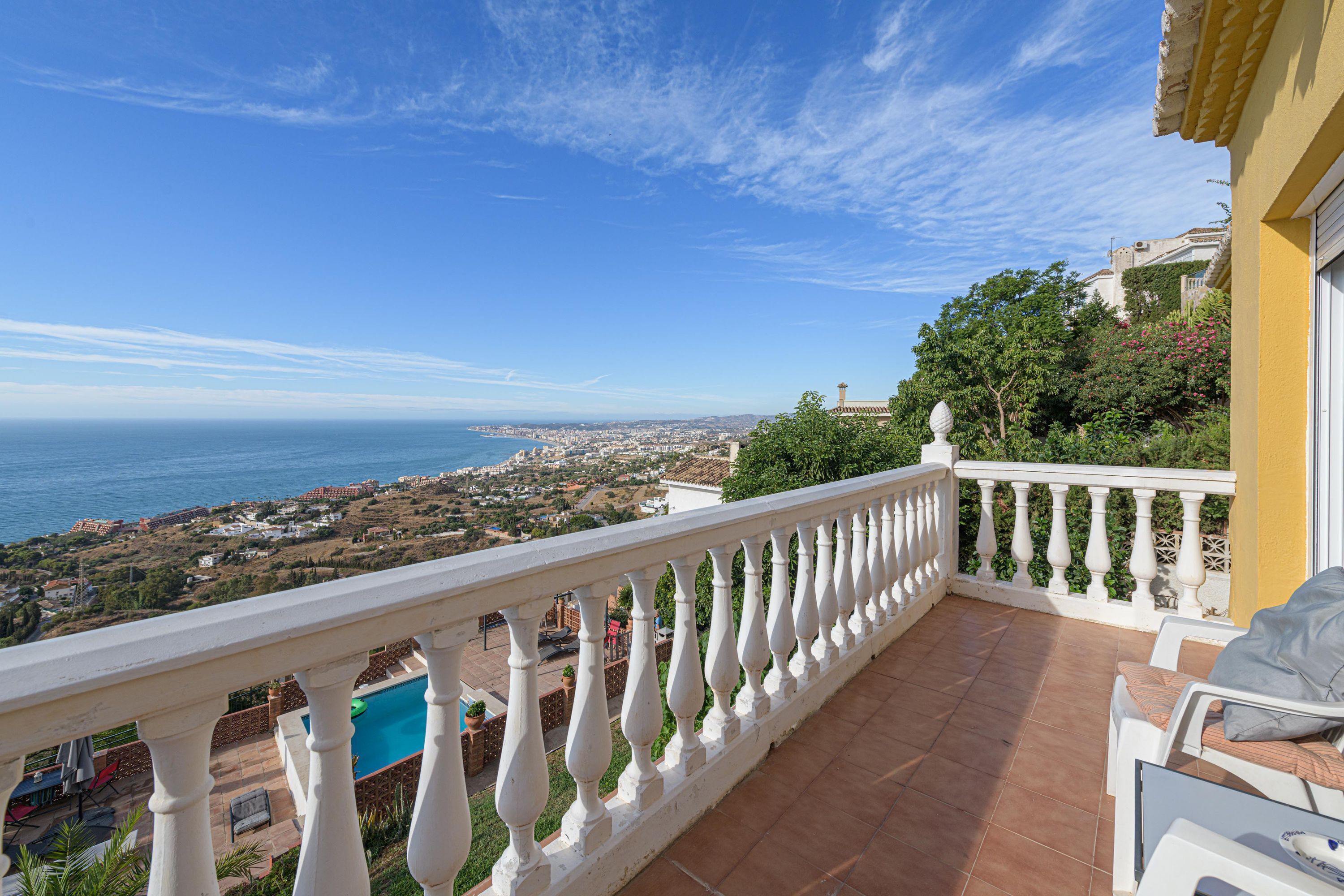 A balcony with a white balustrade overlooking a coastal town and the sea.