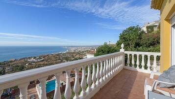 A balcony with a white balustrade overlooking a coastal town and the sea.