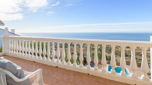 Un balcon doté d’une balustrade blanche, offrant une vue sur une piscine et sur la côte.