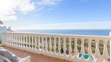 A balcony with a white balustrade overlooking a pool and a coastal view.