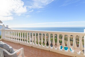 Un balcone con ringhiera bianca che si affaccia su una piscina e sulla costa.